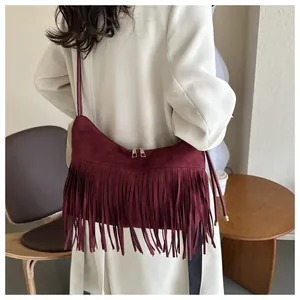 Detail of burgundy fringe crossbody bag on cream coat with dual zippers and suede texture
