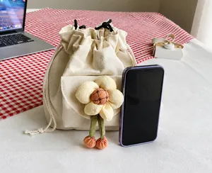 Detail view of mini beige canvas bucket bag with floral accent and smartphone for scale