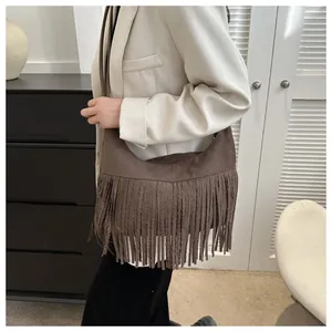 Detail of dark brown suede crescent bag with long fringe accents on model's shoulder