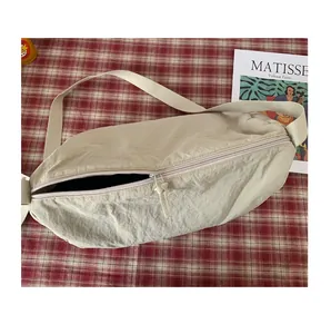 Gros plan du sac en croissant plissé beige avec large bandoulière sur tissu à carreaux