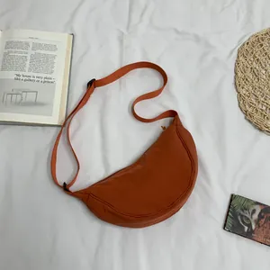 Platliggende weergave van een karamel nylon halve maan tas met minimalistische rekwisieten