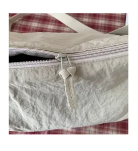 Gros plan du sac en toile crème avec fermeture éclair fluide et tirette à nœud élégante
