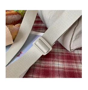 Détail de la bandoulière réglable et de la boucle sur un sac en toile plissé beige