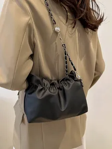 Chic black pleated cloud bag with metallic chain strap worn over a beige blazer