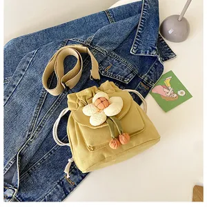 Detail of yellow canvas bucket bag featuring 3D white flower and orange pompom charm