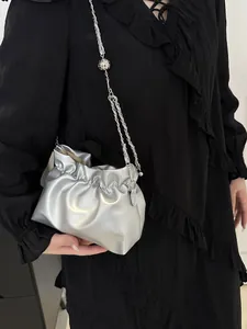 Silver pleated cloud handbag with metallic chain strap shown against a black dress