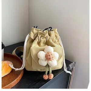 Detail of canvas drawstring bucket bag featuring a large white plush flower decoration