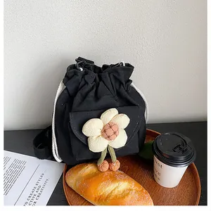 Detail view of canvas bucket bag with plush flower charm on a cafe wooden table