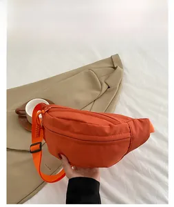 Close-up of orange waterproof nylon crossbody bag with adjustable wide strap on casual outfit