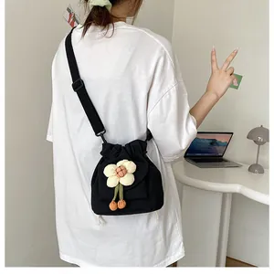 Detail of a black canvas drawstring bucket bag featuring a large 3D white flower charm