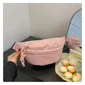 Detail of light pink crescent nylon chest bag with woven zipper pull on a stylish desk