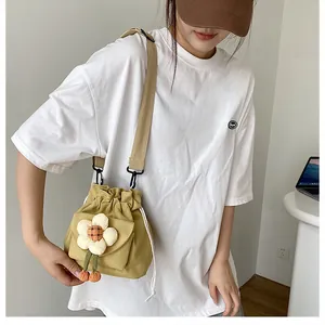 Detail of mustard yellow canvas bucket bag featuring a white flower plush ornament and strap