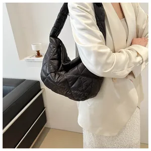 Detail of black quilted puffer hobo bag with large rhombic stitching shown on model