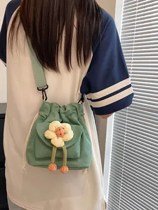 Green canvas drawstring bucket bag with yellow flower and orange plush ball charms