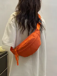 Bright orange crescent nylon crossbody bag worn by a model against a white wall