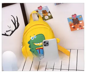 Mini yellow toddler backpack with green dinosaur print shown next to a phone for scale