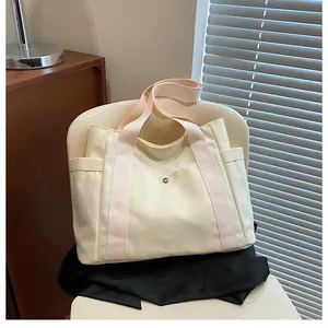 Detail of canvas tote bag featuring cream fabric, pink handles, and a metal button pocket
