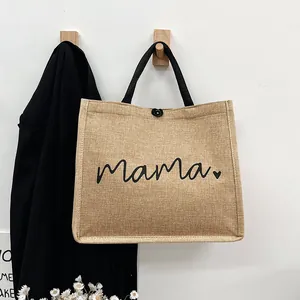 Minimalist jute tote bag with black mama script text hanging on a wooden wall hook