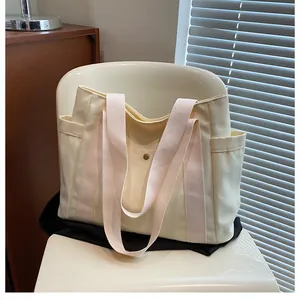 Detail of off-white canvas tote bag featuring pink woven straps and a metal snap button
