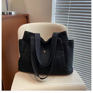 Detail of black canvas tote bag with side pockets and golden snap button on a chair