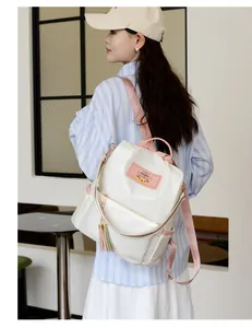 Vue latérale du sac à dos Oxford blanc avec accents roses et pompons sur un mannequin