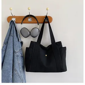 Detail of black canvas tote bag featuring reinforced straps and side storage pockets