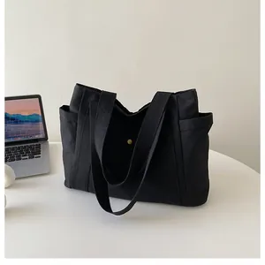 Detalle del bolso tote negro de lona con bolsillos laterales y cierre magnético dorado