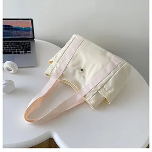 Bolso de lona beige con asas rosas y bolsillos, mostrado en un escritorio con un portátil
