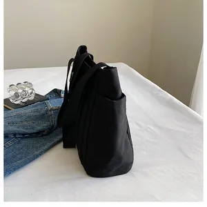 Vista detallada del bolso tote de lona negra con bolsillo lateral y correa de hombro ancha