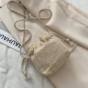 Handwoven beige straw bucket bag with drawstring closure and crossbody strap