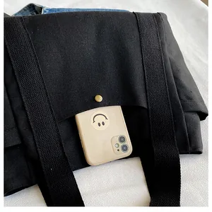 Detalle del bolso tote de lona negra con bolsillo funcional y broche de presión de latón