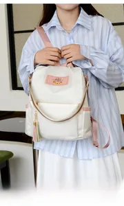 Détail du sac à dos blanc en Oxford avec sangles roses et pompons décoratifs bicolores