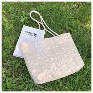 Detailaufnahme der beigen Strohtasche mit Spitzenschleife und Blumenstickerei