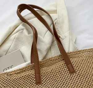 Detailed view of woven straw tote bag with brown faux leather handles and fine stitching