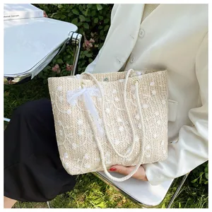 Detailansicht der beigen Strohtasche mit Blumenstickerei und weißer Spitzenschleife