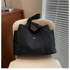 Bolso tote negro minimalista de lona con correas anchas y bolsillos frontales funcionales