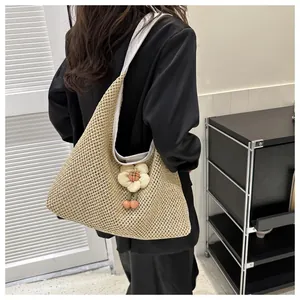 Detalle de bolso tote de paja tejido a mano con colgante de flor y correa blanca