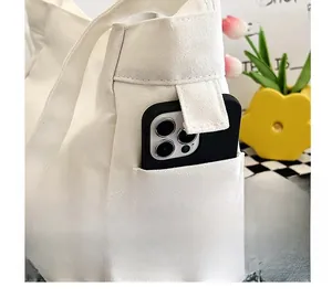 Détail d'un sac cabas en toile montrant la poche latérale contenant un smartphone