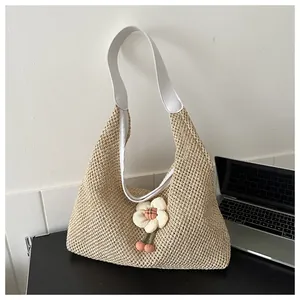 Detalle del bolso tote beige tejido a mano con correa de cuero blanco y colgante de flores