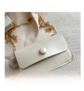 Detail of cream white pebbled leather crossbody bag with gold chain and round buckle