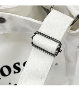 Détail macro du sac en toile blanche montrant la boucle en métal noir et la bandoulière