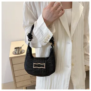 Detail of black crocodile pattern leather handbag with knot handle and gold metal buckle