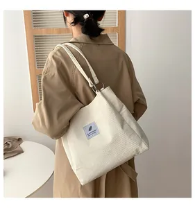 Detail of cream corduroy tote bag featuring blue feather label and metal ring strap