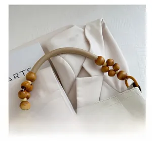 Detail of cream tote bag featuring woven rope handle with decorative brown wooden beads