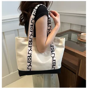 Détail du sac cabas en toile avec base contrastée et bandoulière à logo dans un salon