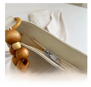 Close-up of cream crossbody bag featuring smooth metal zipper and decorative wood beads