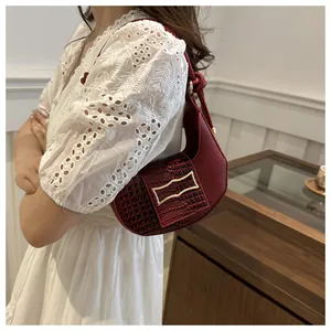 Detail of wine red crescent bag featuring crocodile embossed flap and gold metal buckle