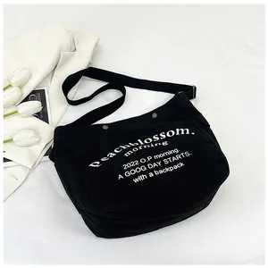 Détail d'un sac bandoulière en toile noire avec lettrage blanc et sangle réglable