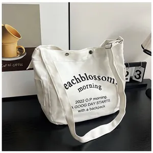 Vue détaillée du sac fourre-tout en toile blanche avec texte et poche latérale
