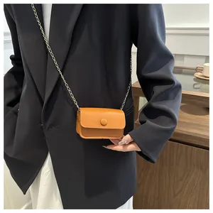 Close-up of a mini brown leather crossbody bag with gold chain strap on a model